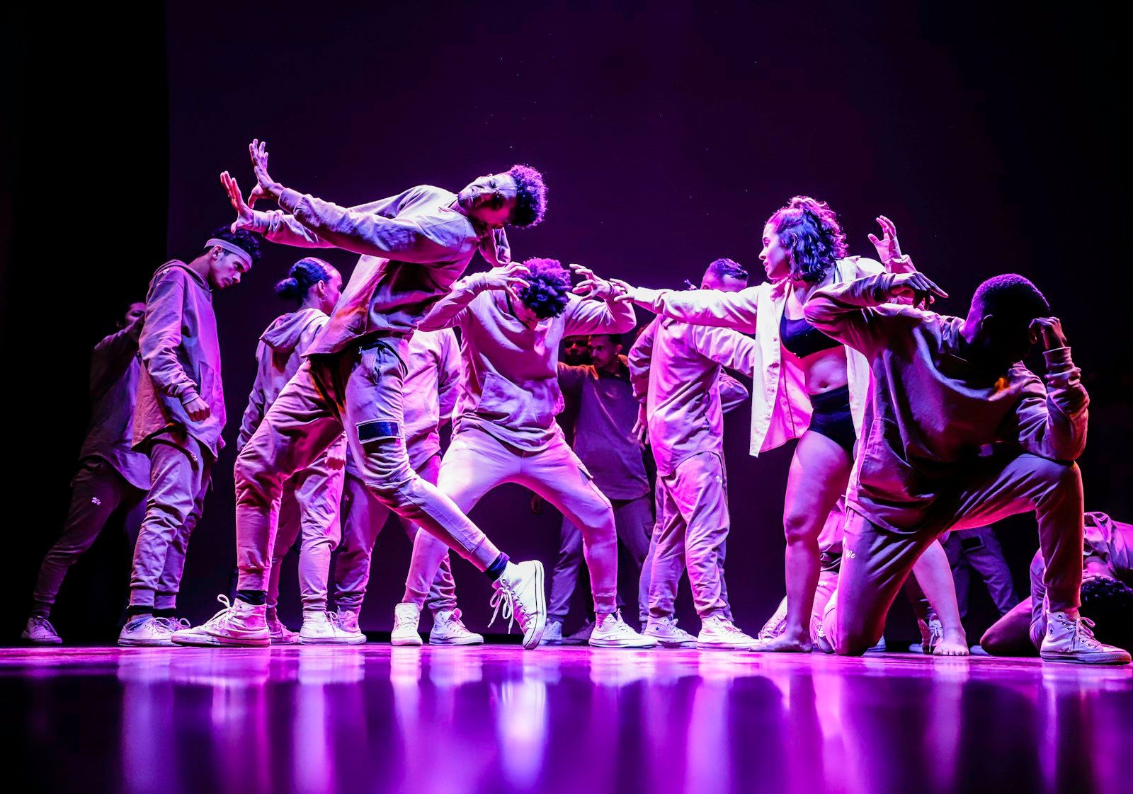 A dance crew performing together on stage under coloured lights.